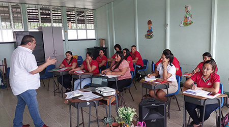 Se muestra un hombre hablando frente a un grupo de personas sentadas en un aula